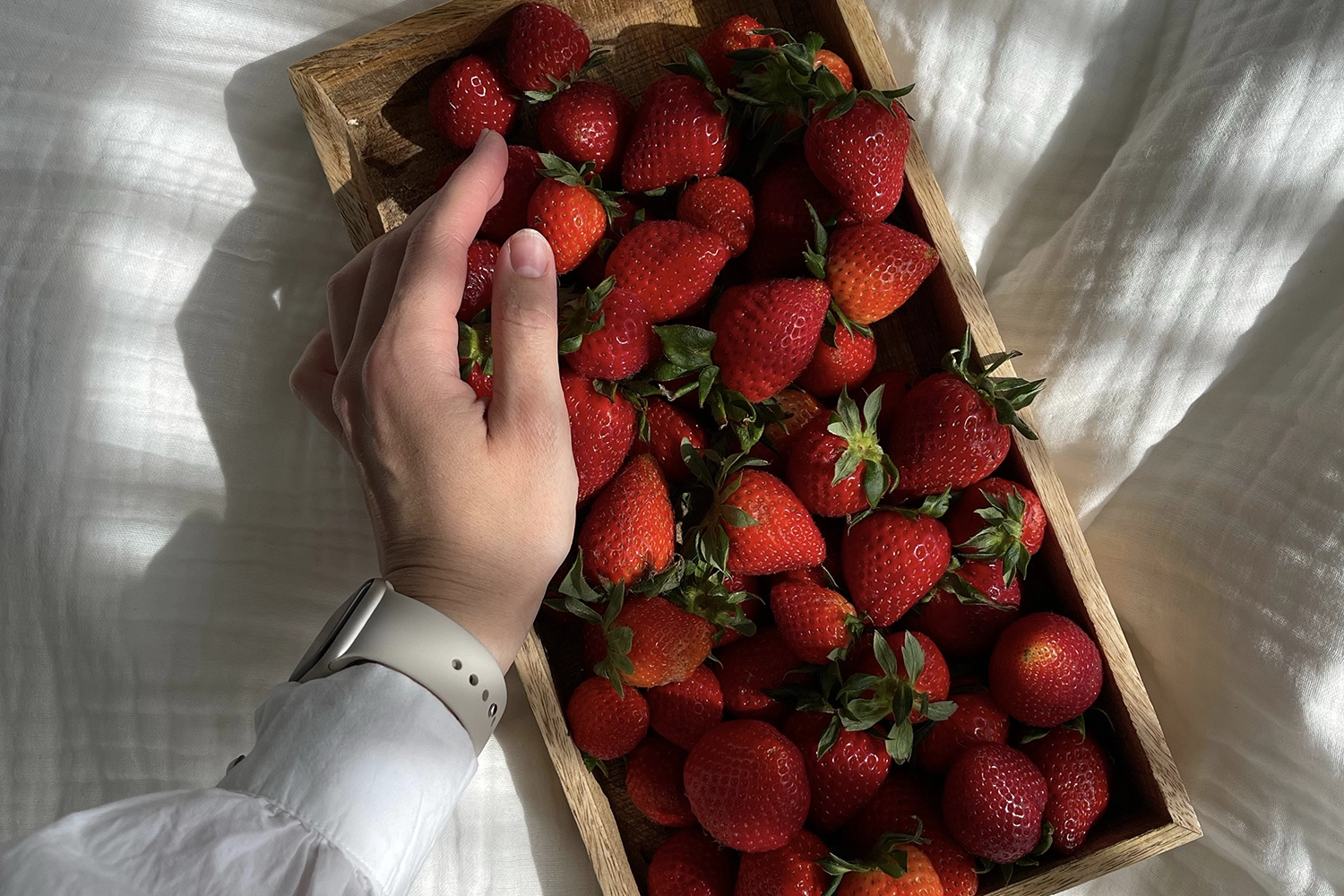 hand reaching for strawberries in a wooden box